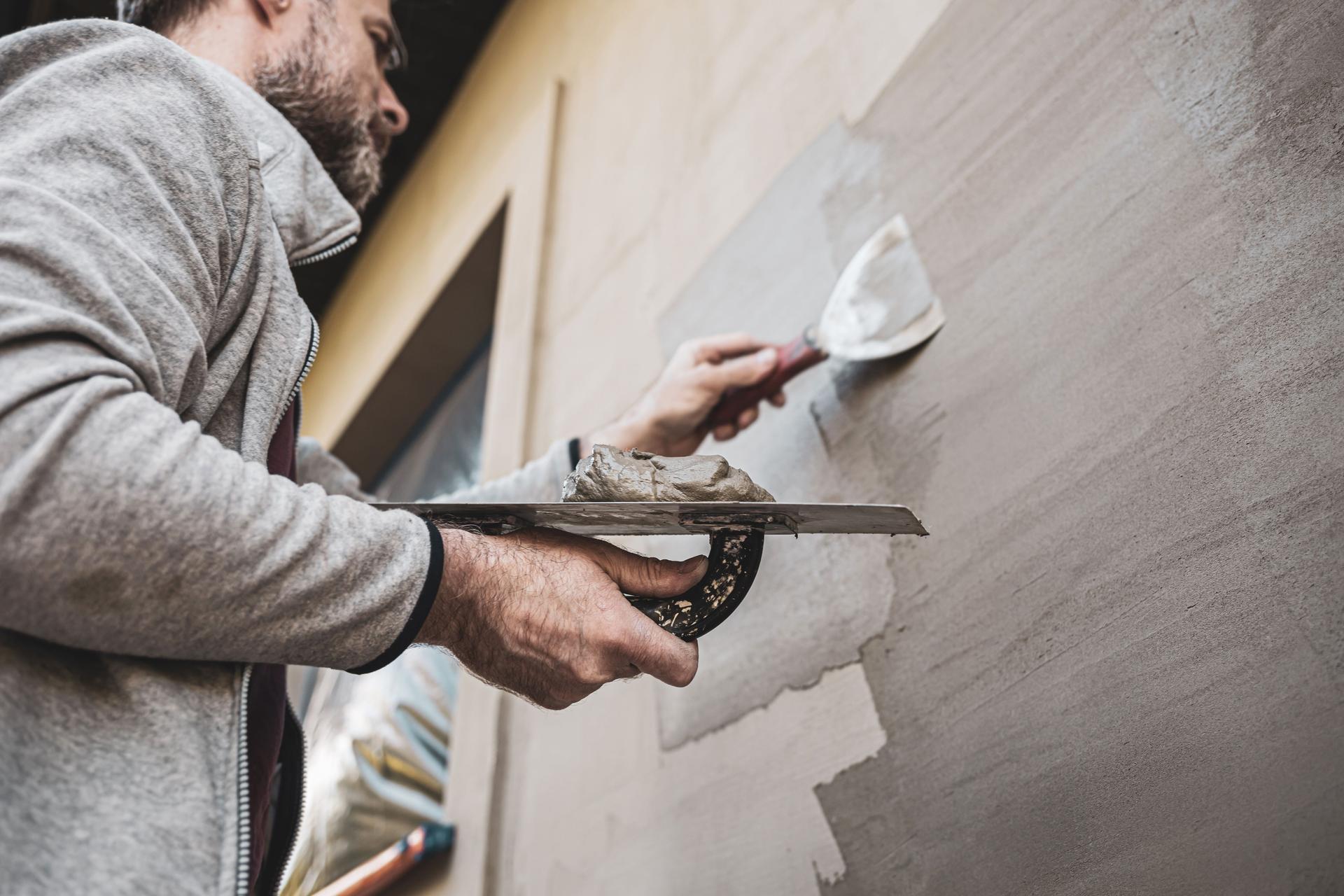 Renovation of the building facade - construction industry. Worker man plastering exterior walls of a house.